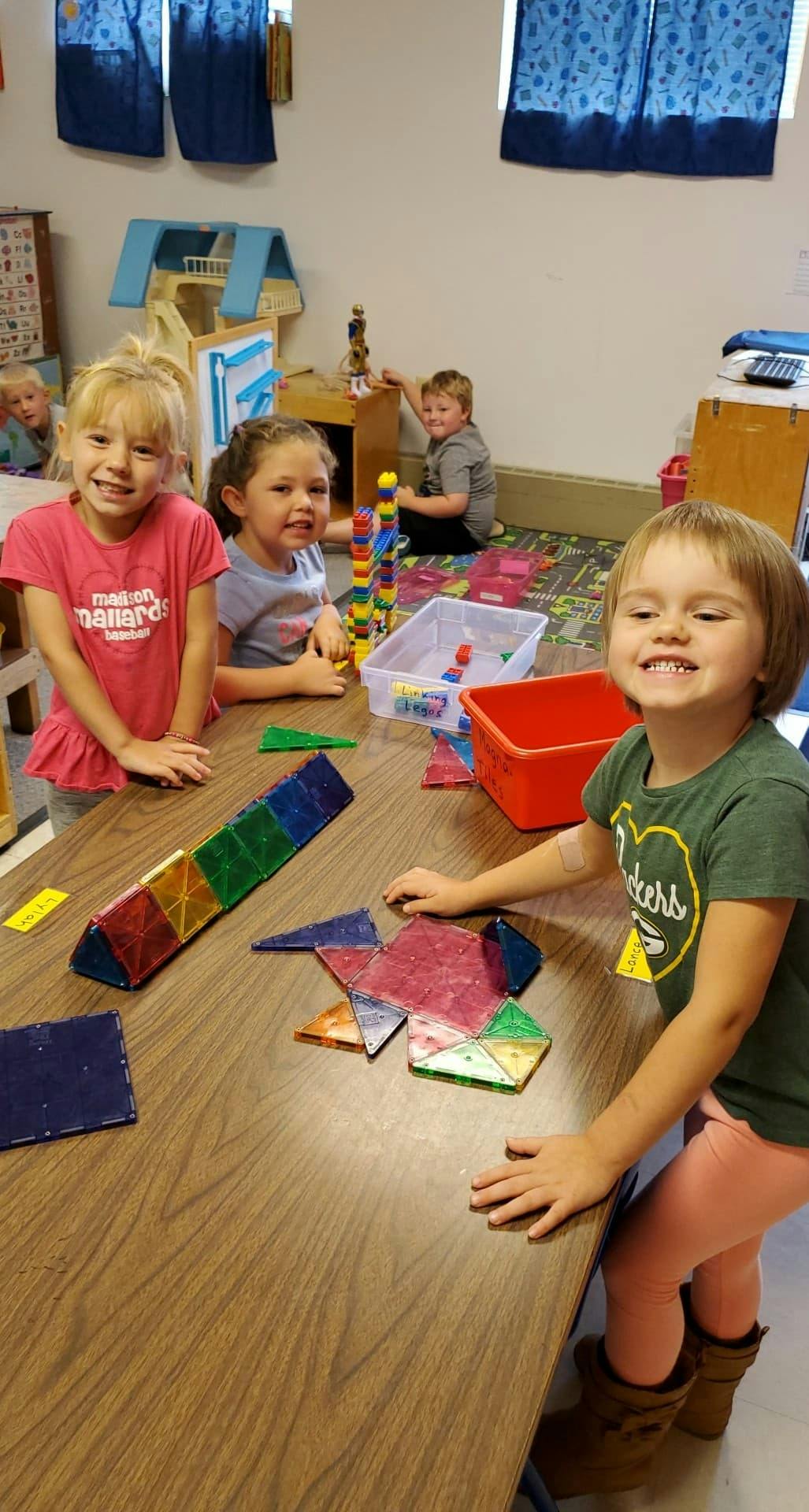 Three children playing with colorful magnetic tiles at a table