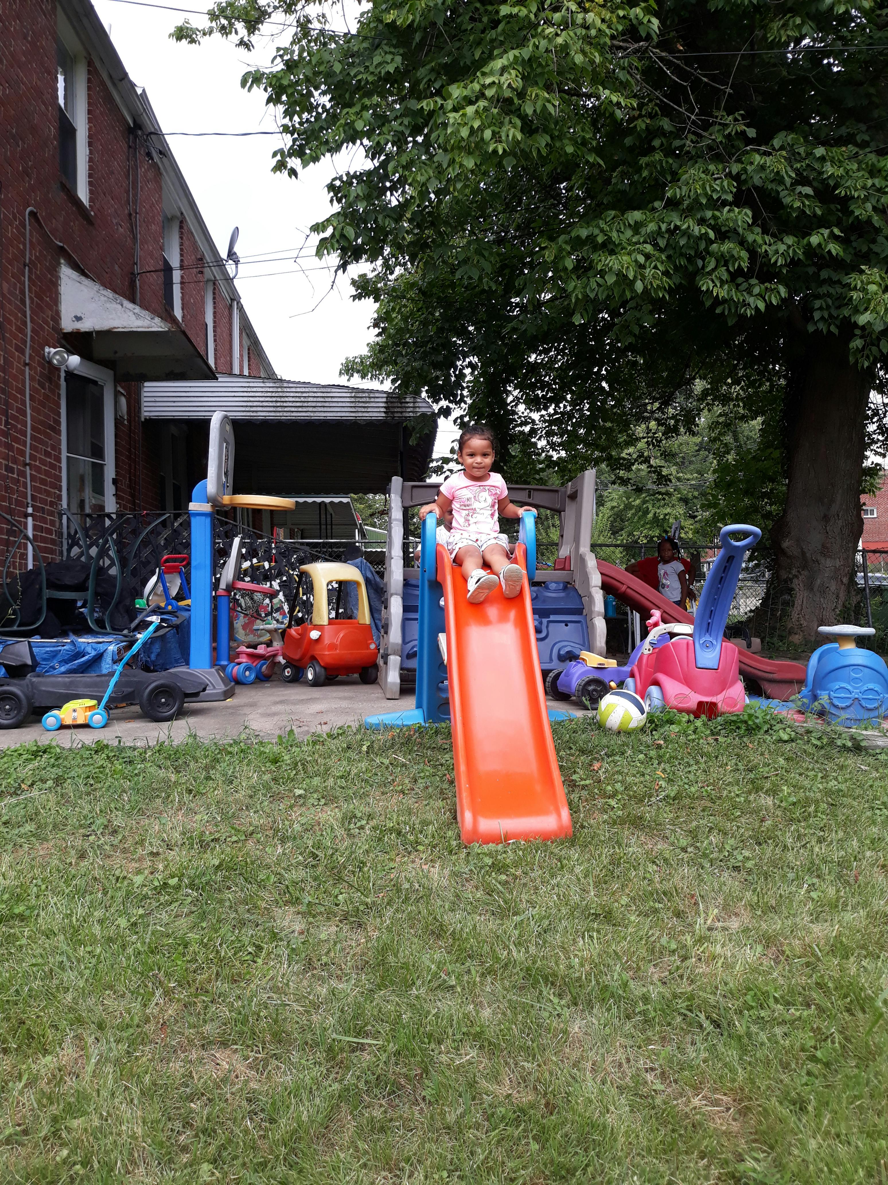 Child sitting at the top of an orange slide in a backyard