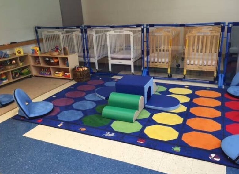 Daycare room with cribs, colorful rug, and soft play equipment