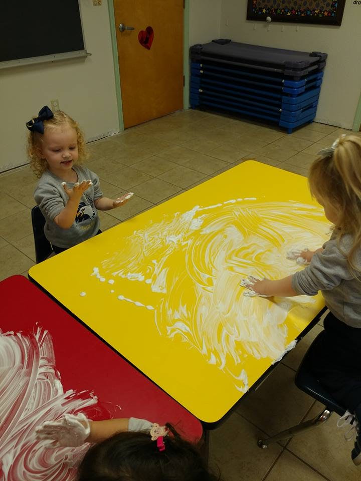 Children playing with shaving cream on tables in a classroom