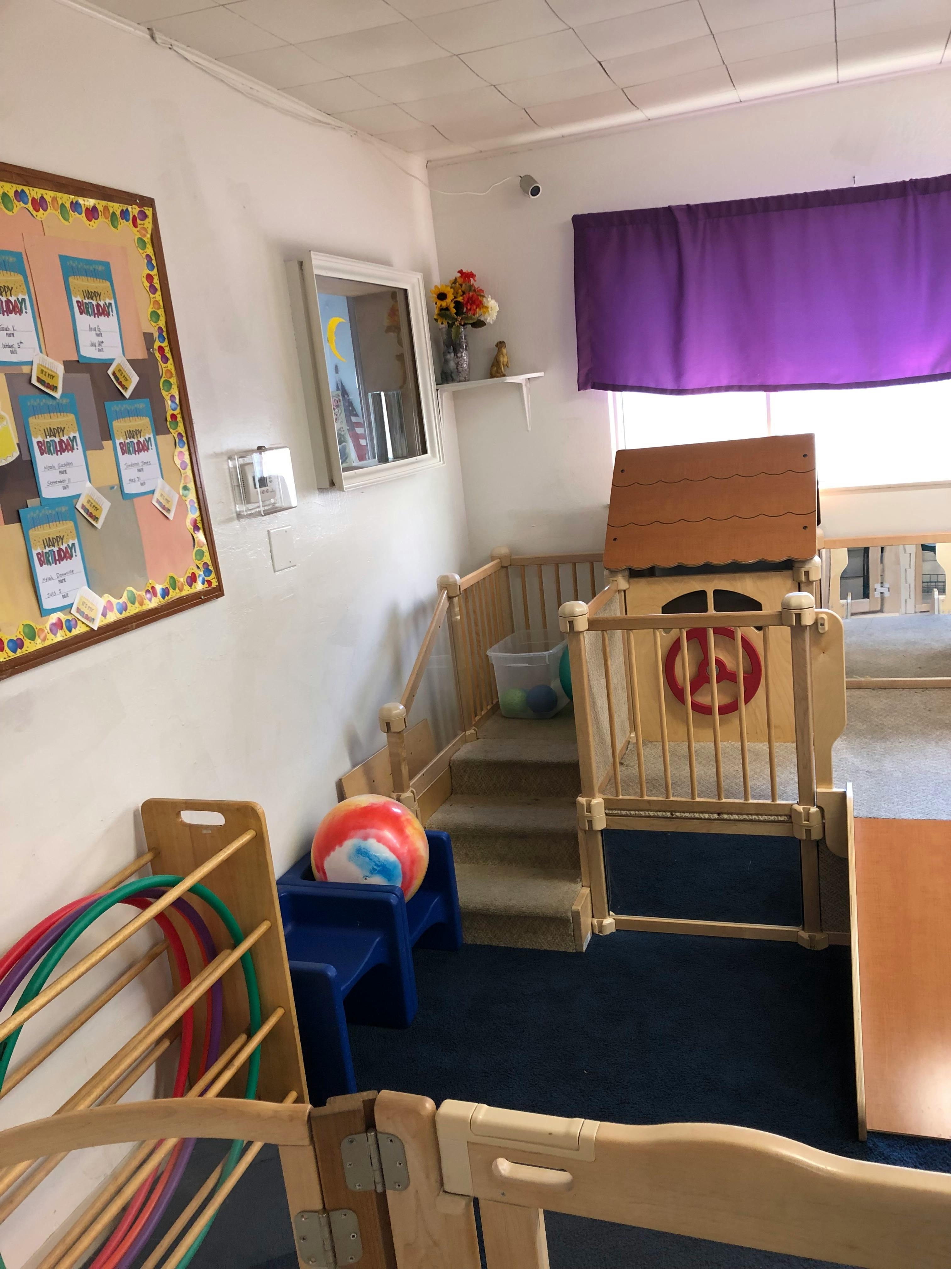 Indoor play area with a small wooden playhouse, stairs, and hula hoops