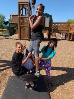 Three children playing on a tire swing at a playground