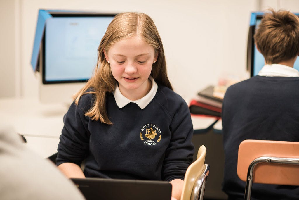 Child in uniform looking down at a laptop in a classroom