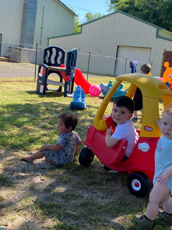 Child sitting on ground, child in toy car, and child standing