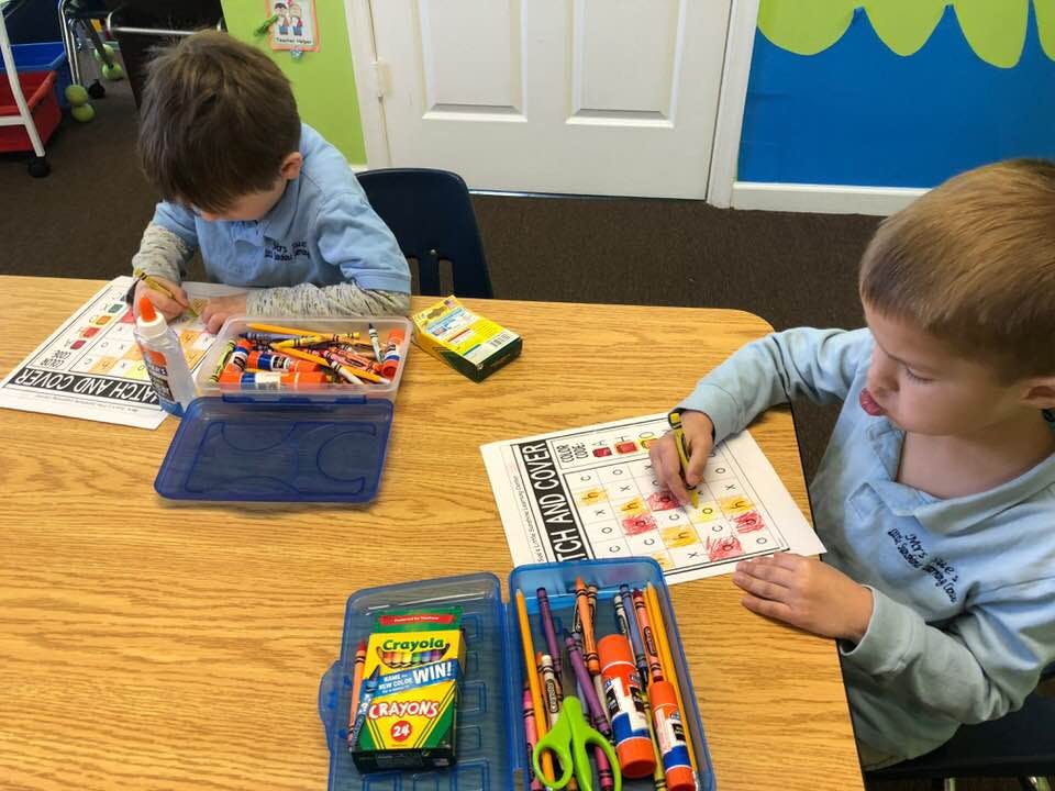 Two children at a table working on papers with art supplies