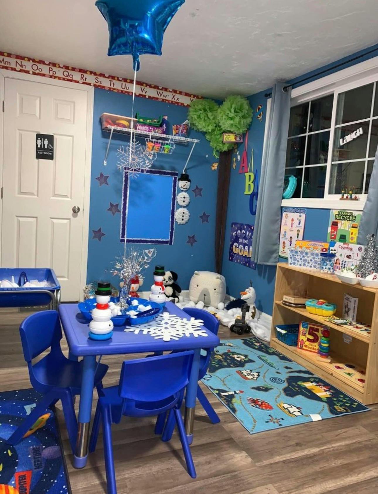 A playroom decorated in blue with a small table and chairs, toys, and educational posters