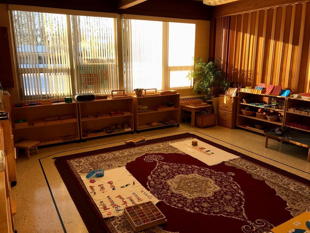 Classroom with large windows, wooden shelves, and a patterned rug