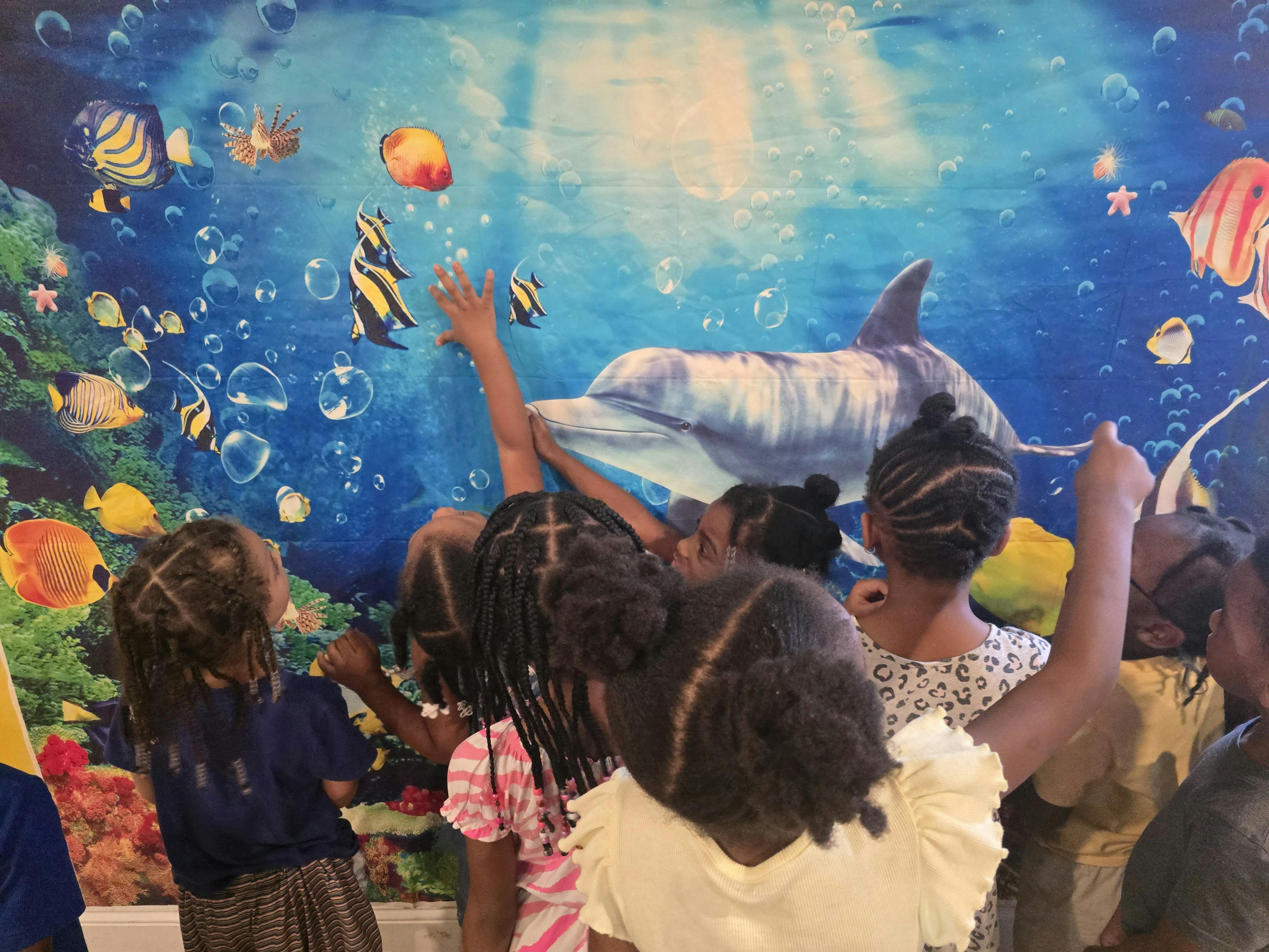 Group of children pointing at an underwater-themed backdrop
