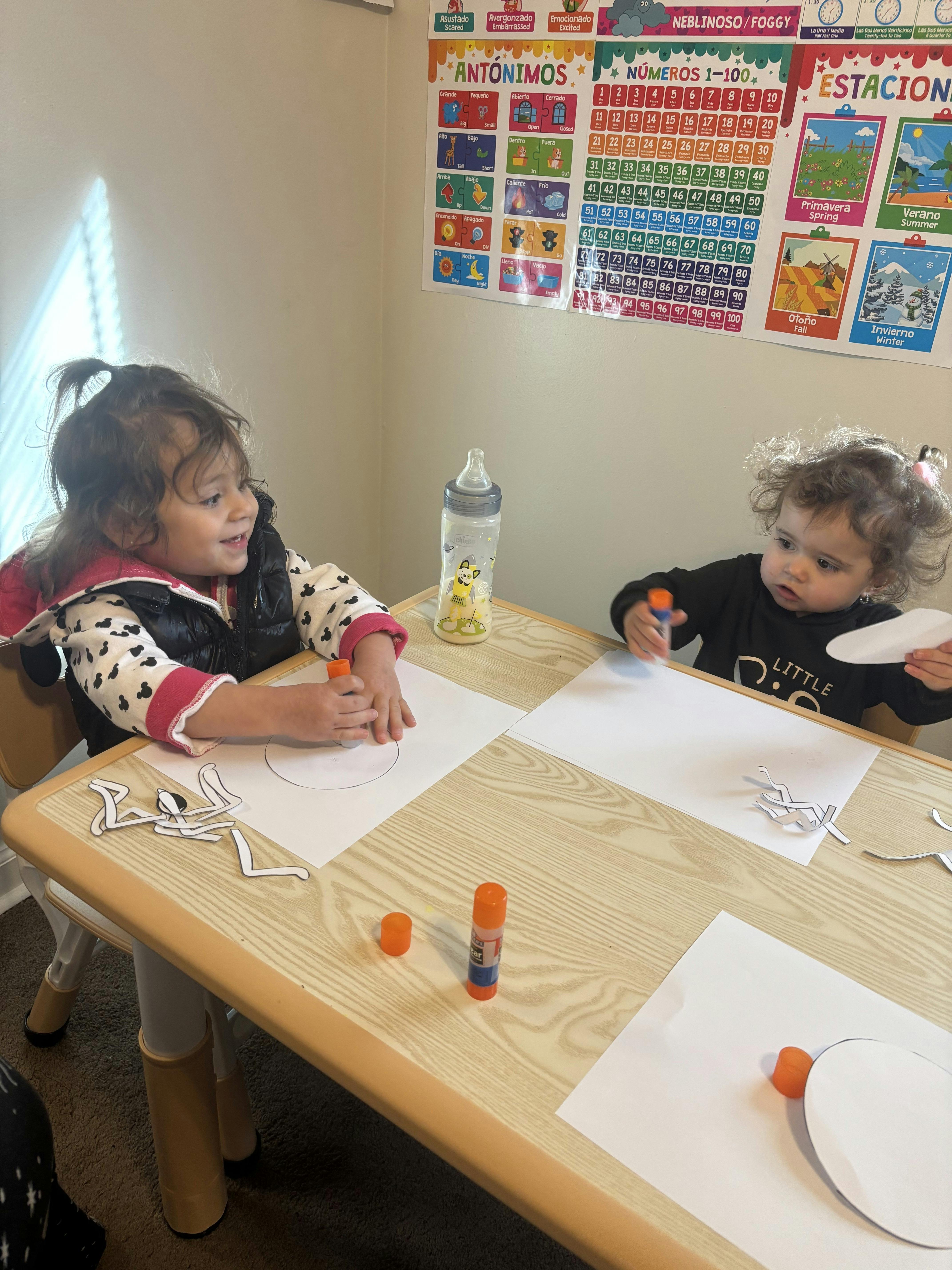 Two children sitting at a table using glue sticks for a paper craft