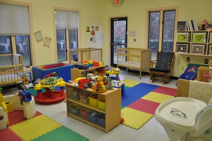 Daycare room with cribs, colorful play mats, and toys