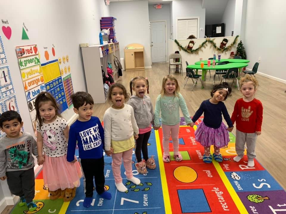 Seven children standing on a colorful rug in a classroom