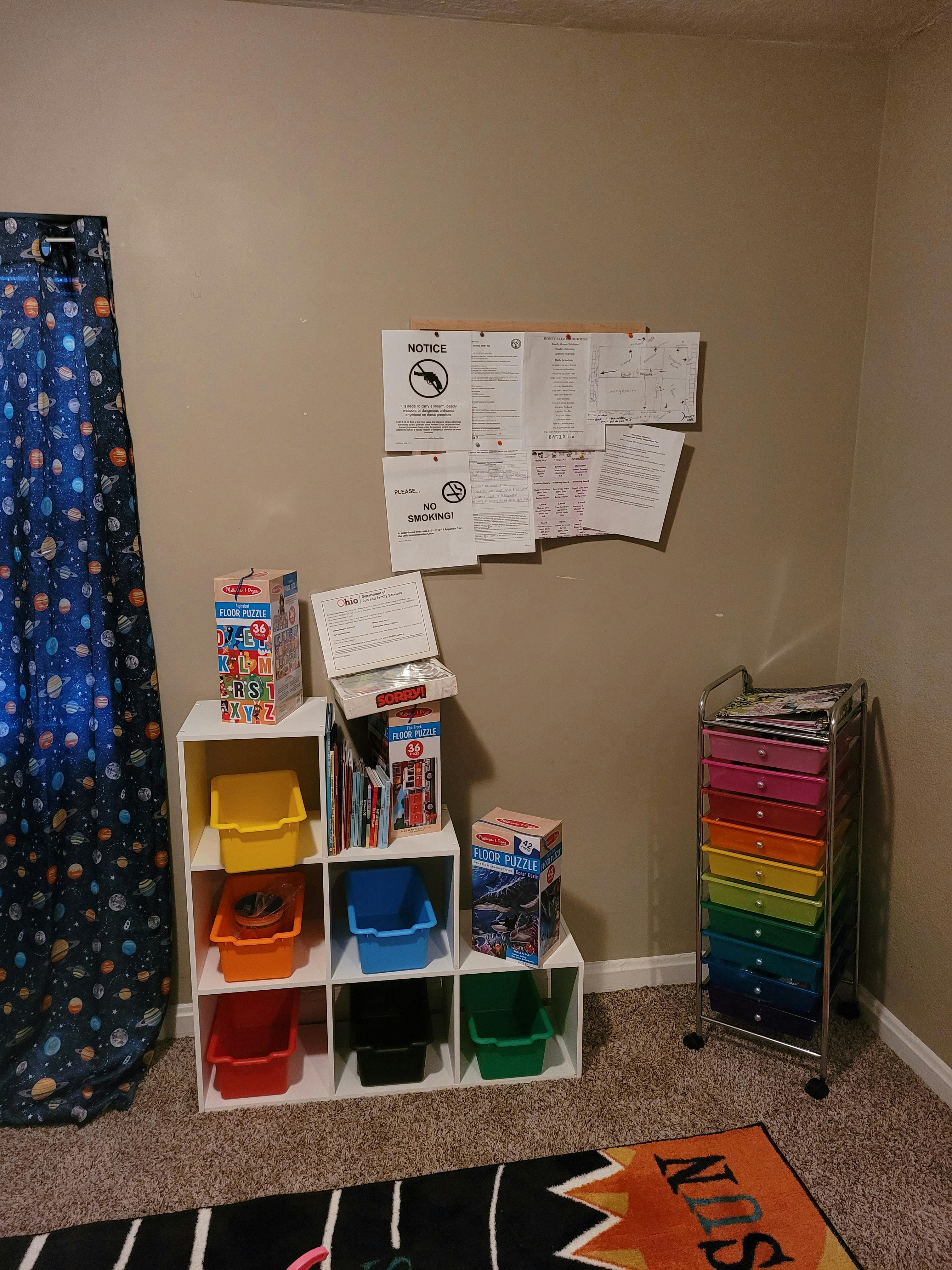 Wall with papers, white storage cubes with colorful bins, and a rainbow drawer cart