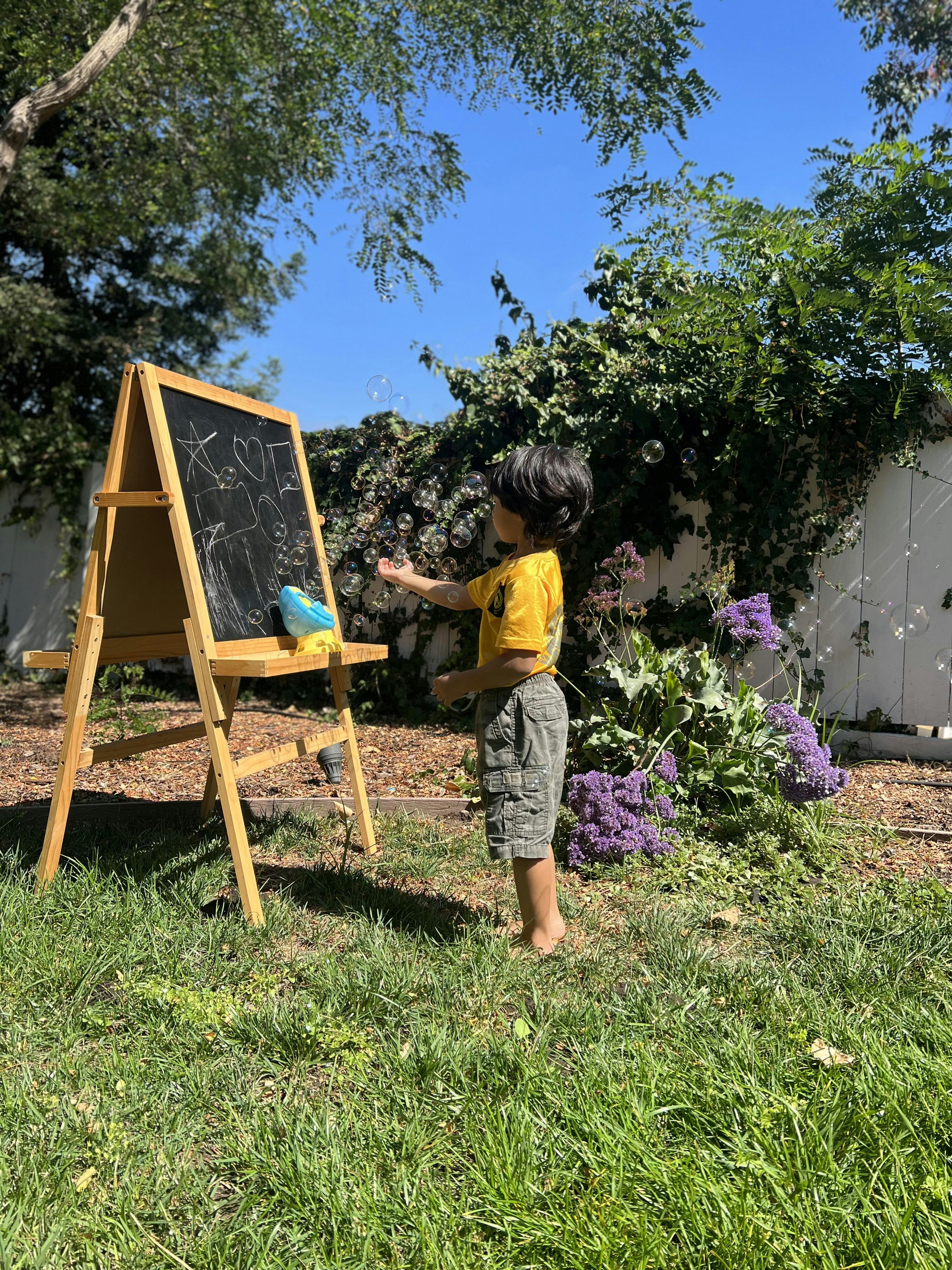 Child standing next to an easel with drawings on a chalkboard