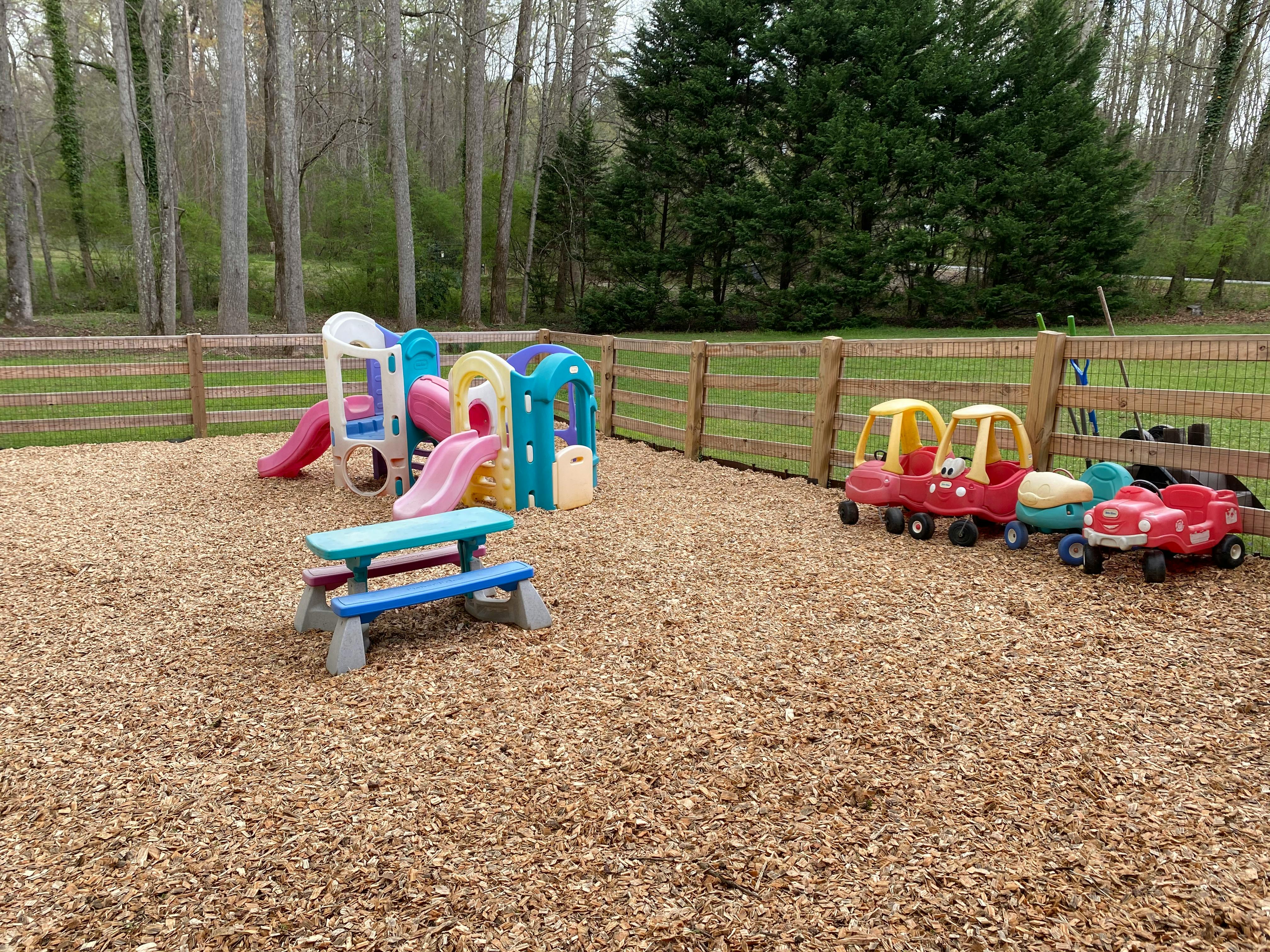 Outdoor playground with slides, playhouses, and ride-on toys on wood chips