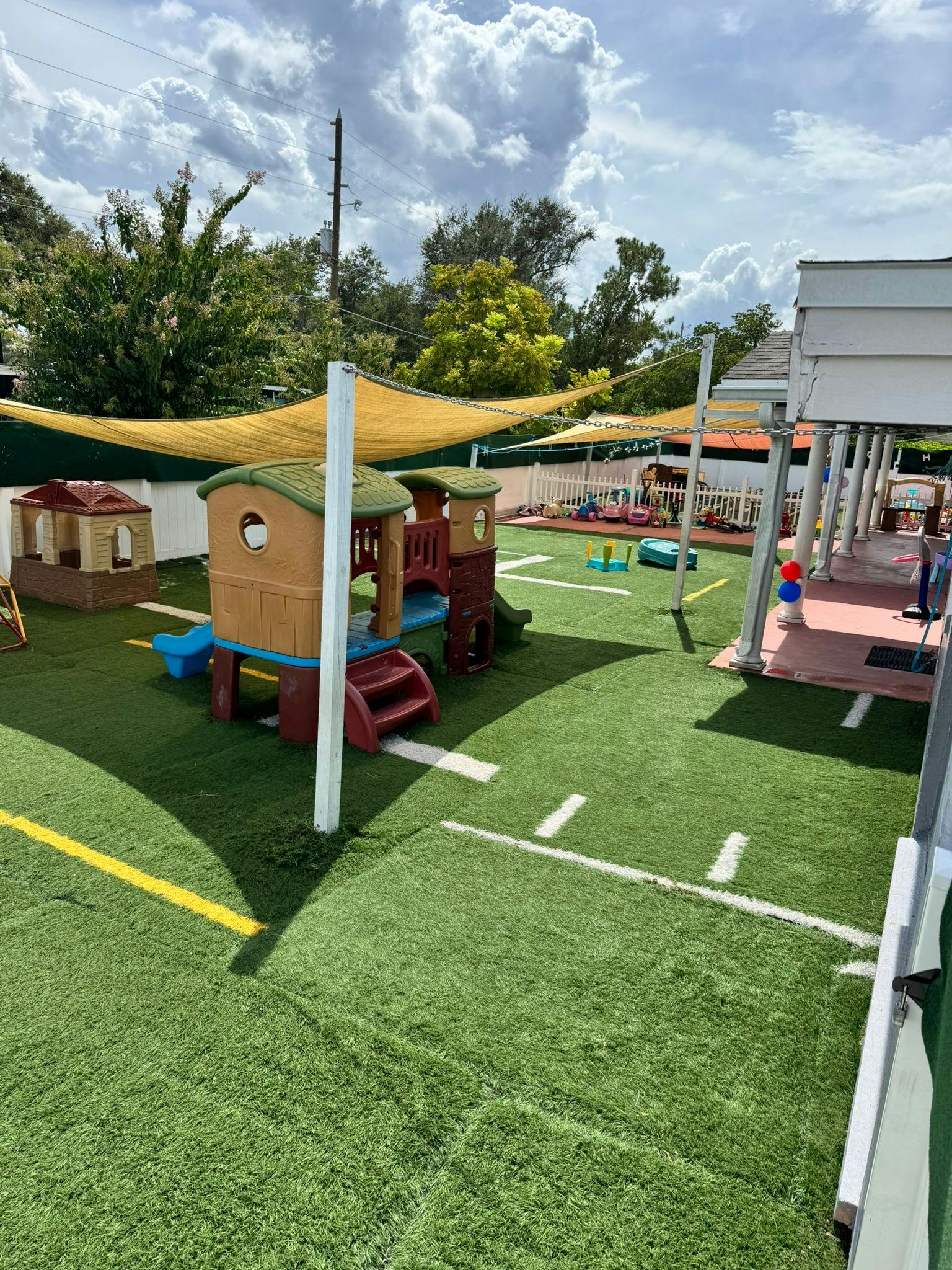 Outdoor playground with artificial turf, play structures, and shade sails
