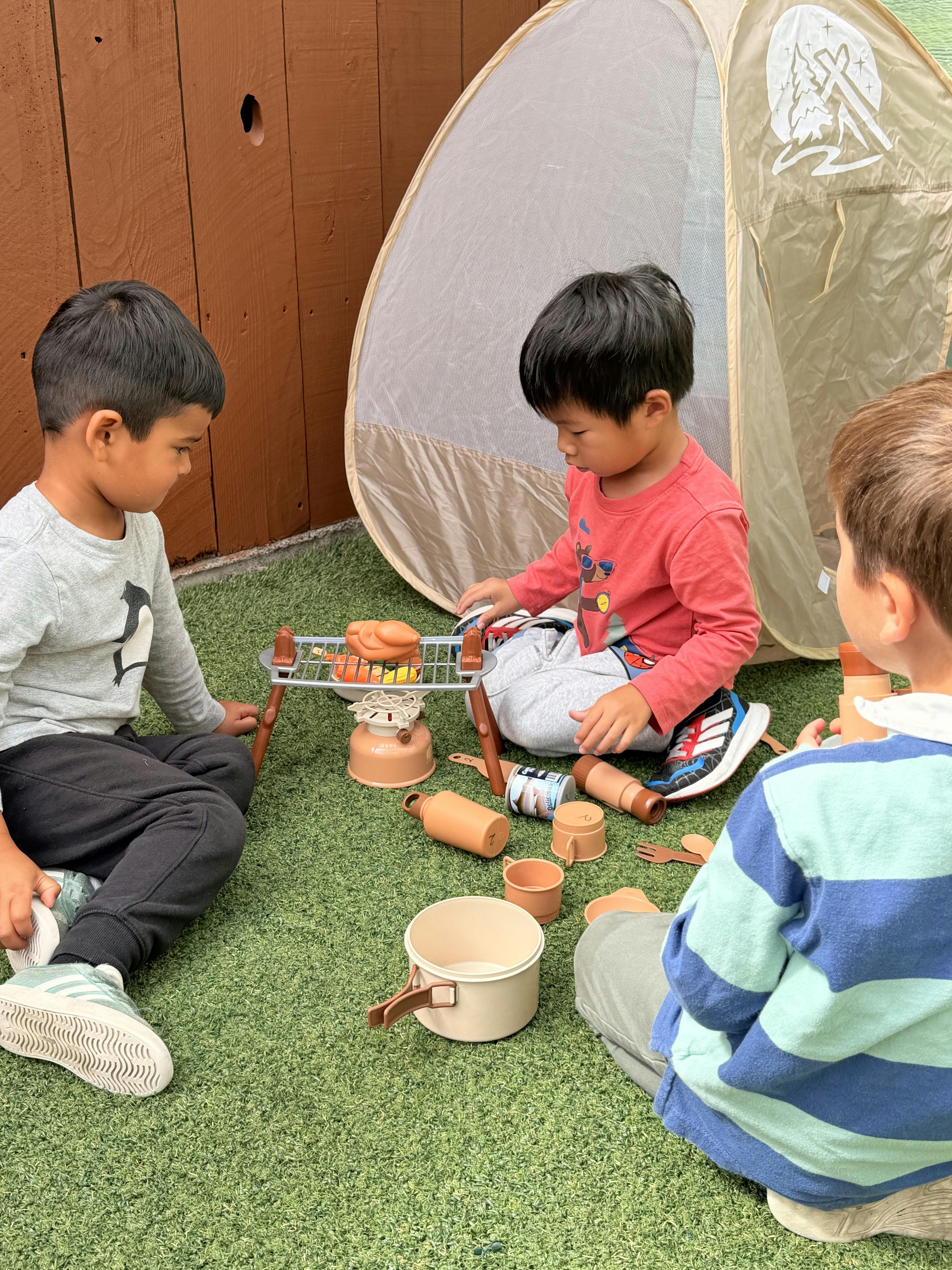Three children playing with toy camping gear and a small play tent
