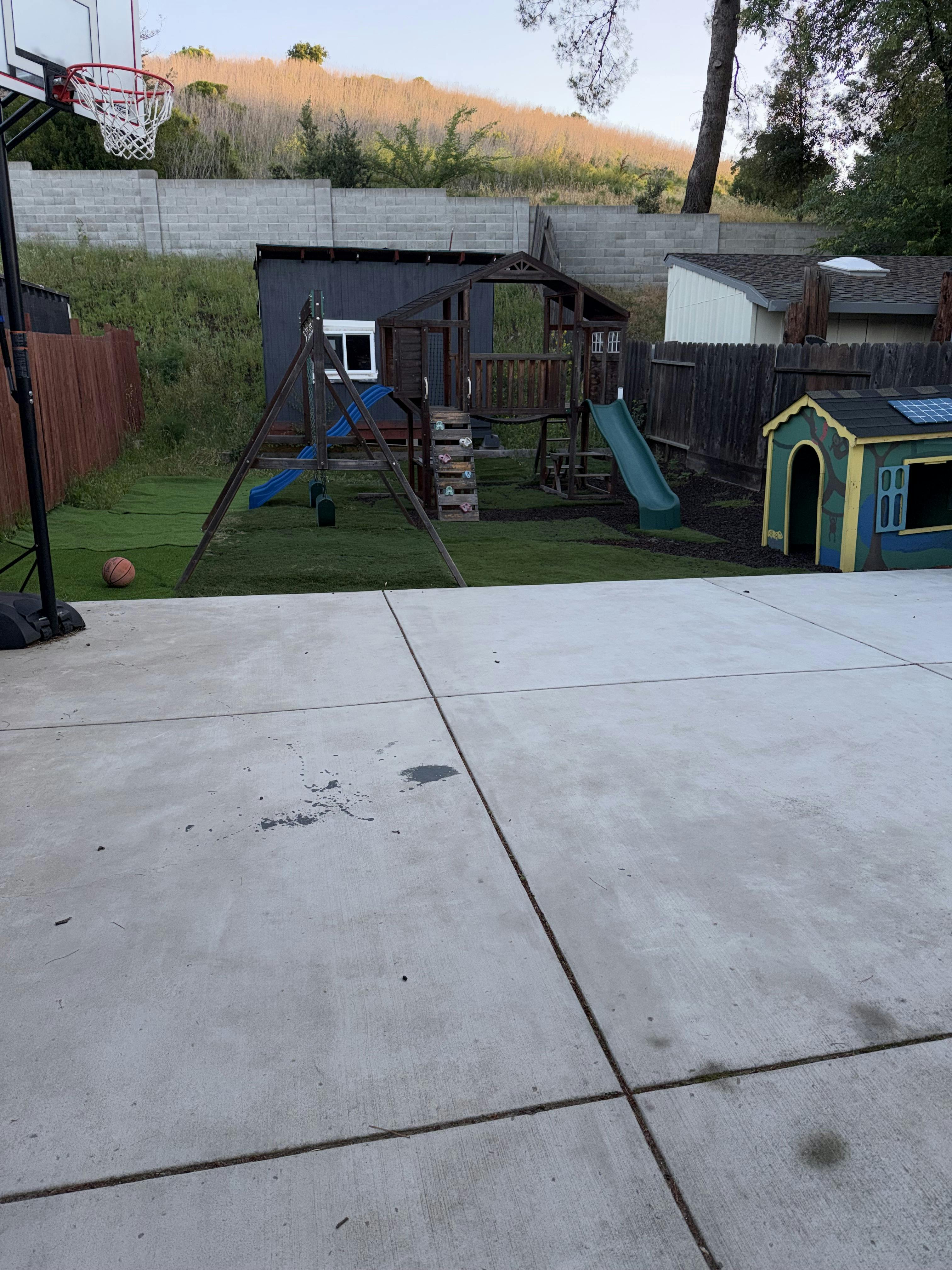 Basketball hoop on a concrete patio next to a wooden playset with slides