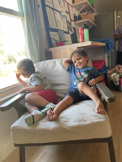 Two children sitting on a chair, one looking out a window