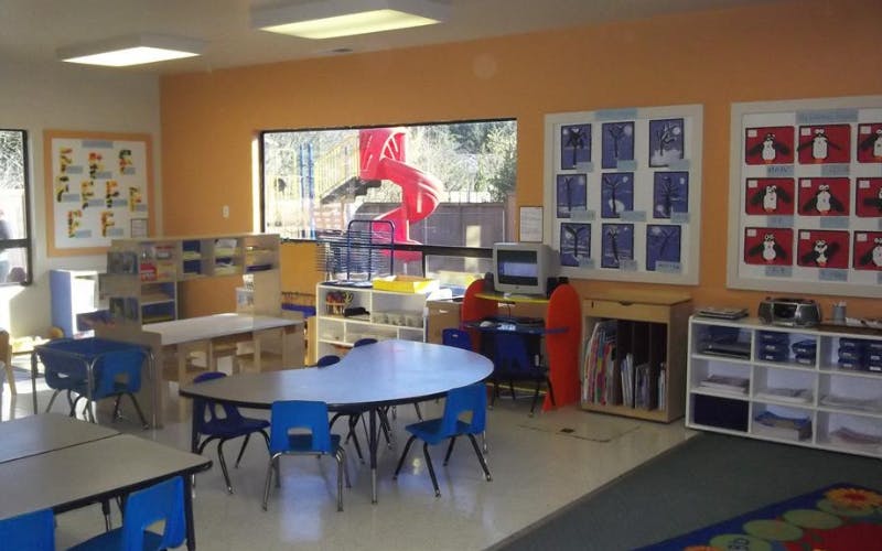 Classroom with tables and chairs, a computer, shelves, and art on orange walls