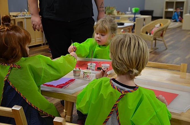 Children in green smocks painting at a table