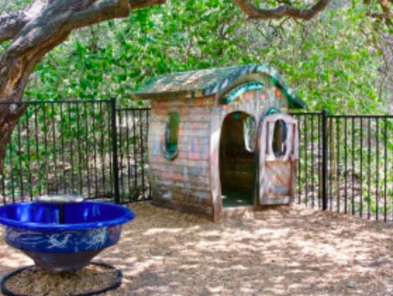 Small wooden playhouse with an open door next to a blue basin