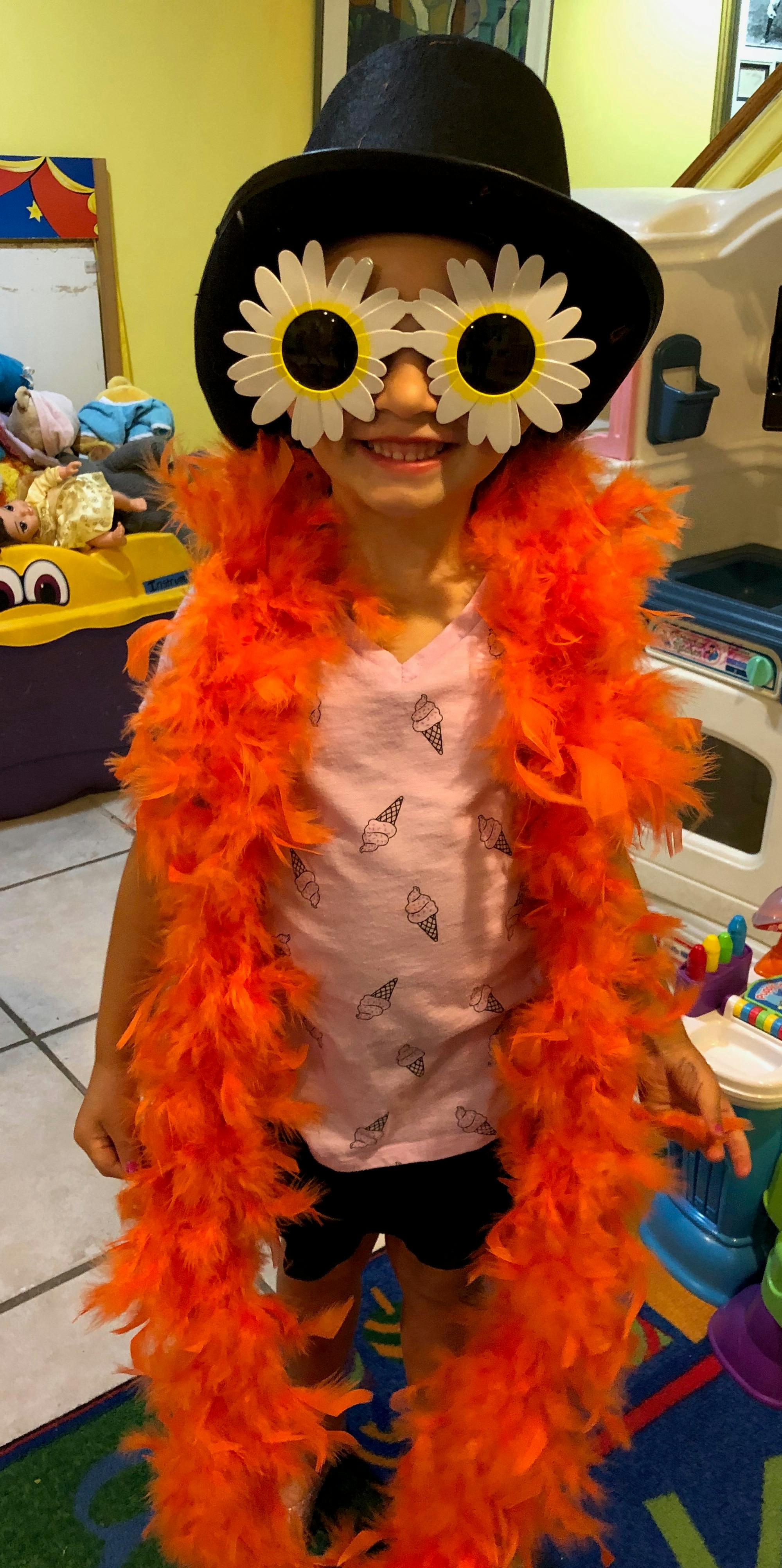Child in a top hat, daisy sunglasses, and an orange feather boa