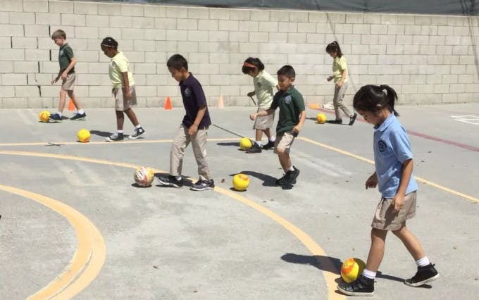 Children playing with soccer balls on a paved surface