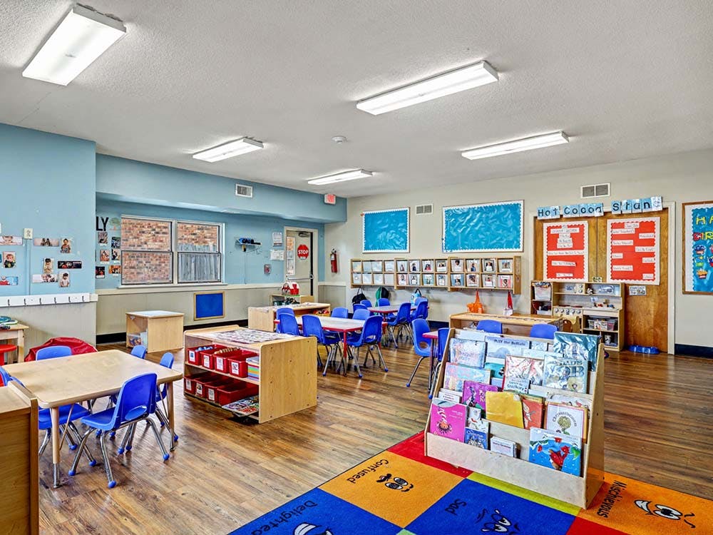 Classroom with small tables and chairs, shelves with books and supplies