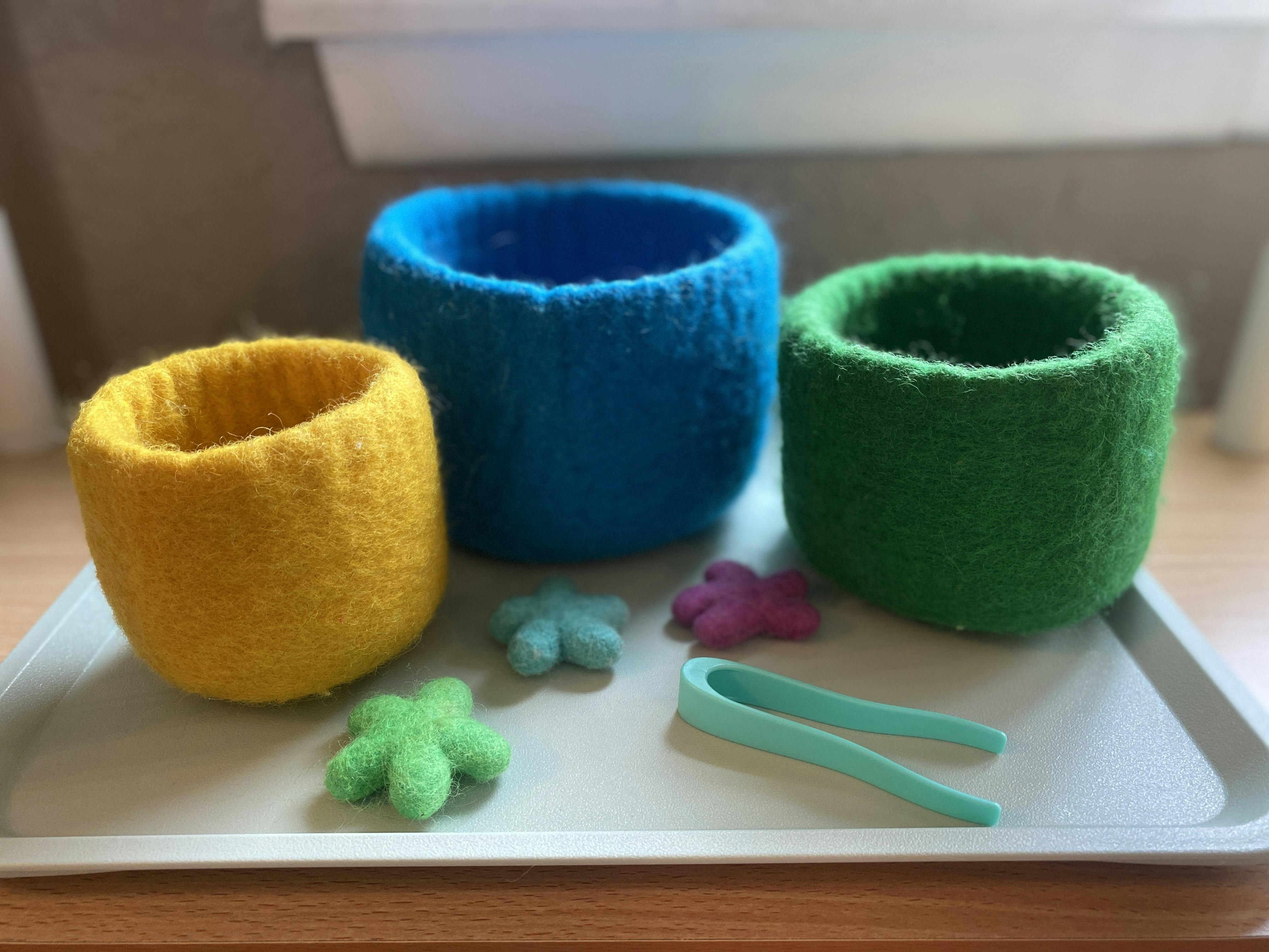 Three felt cups with felt shapes and plastic tongs on a tray
