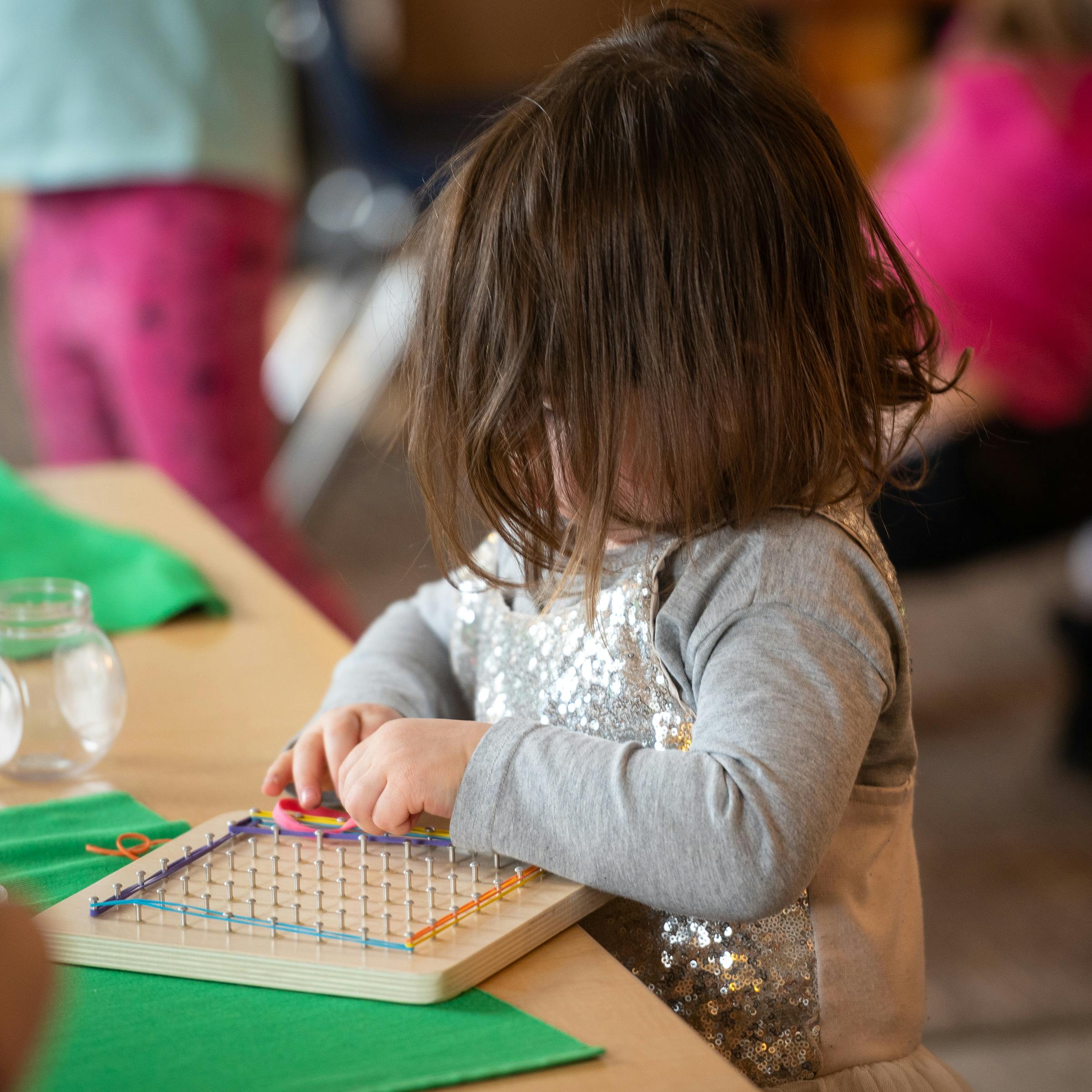 Child playing with a geoboard at a table