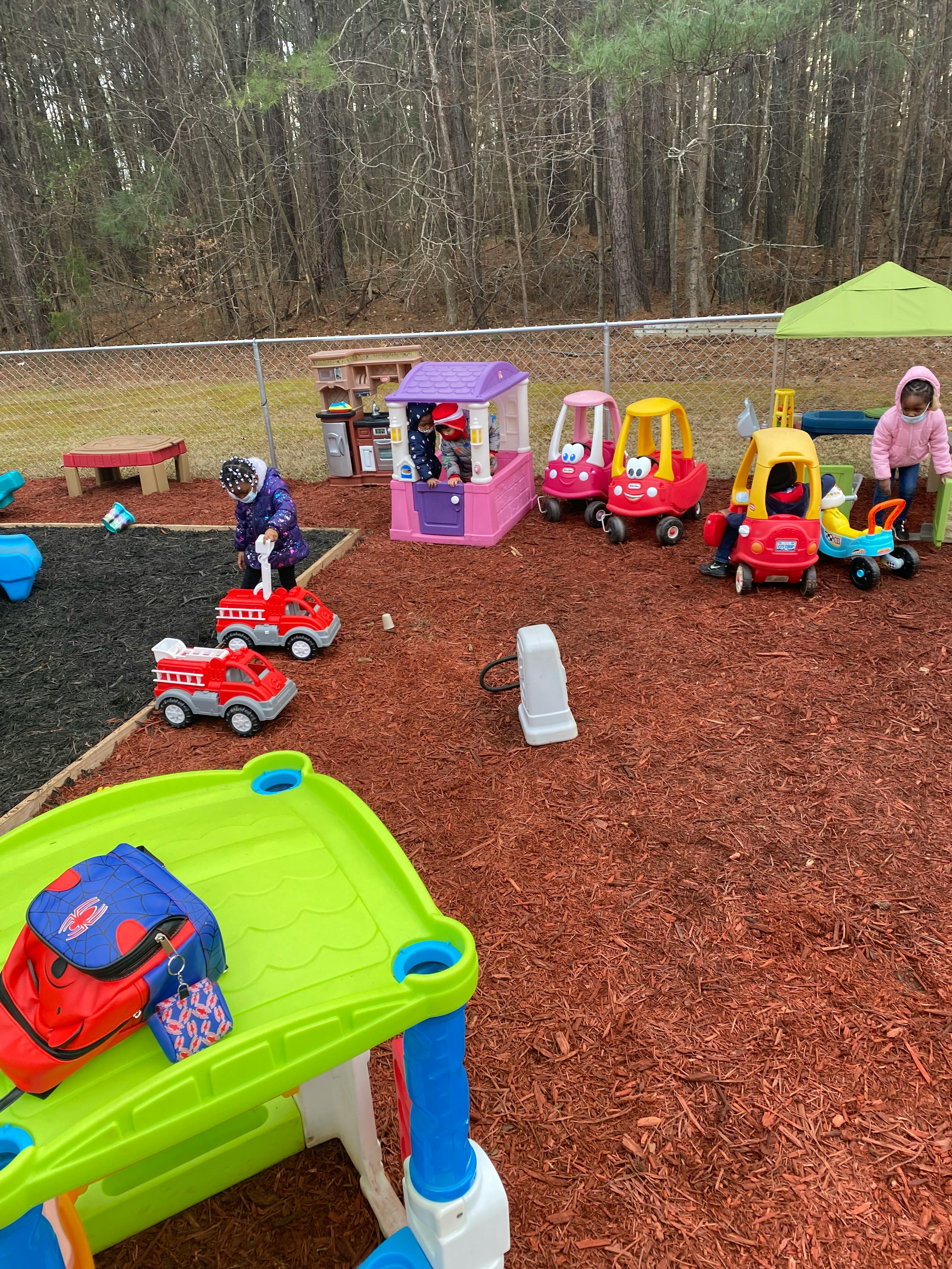 Children playing with toy cars and a playhouse outdoors