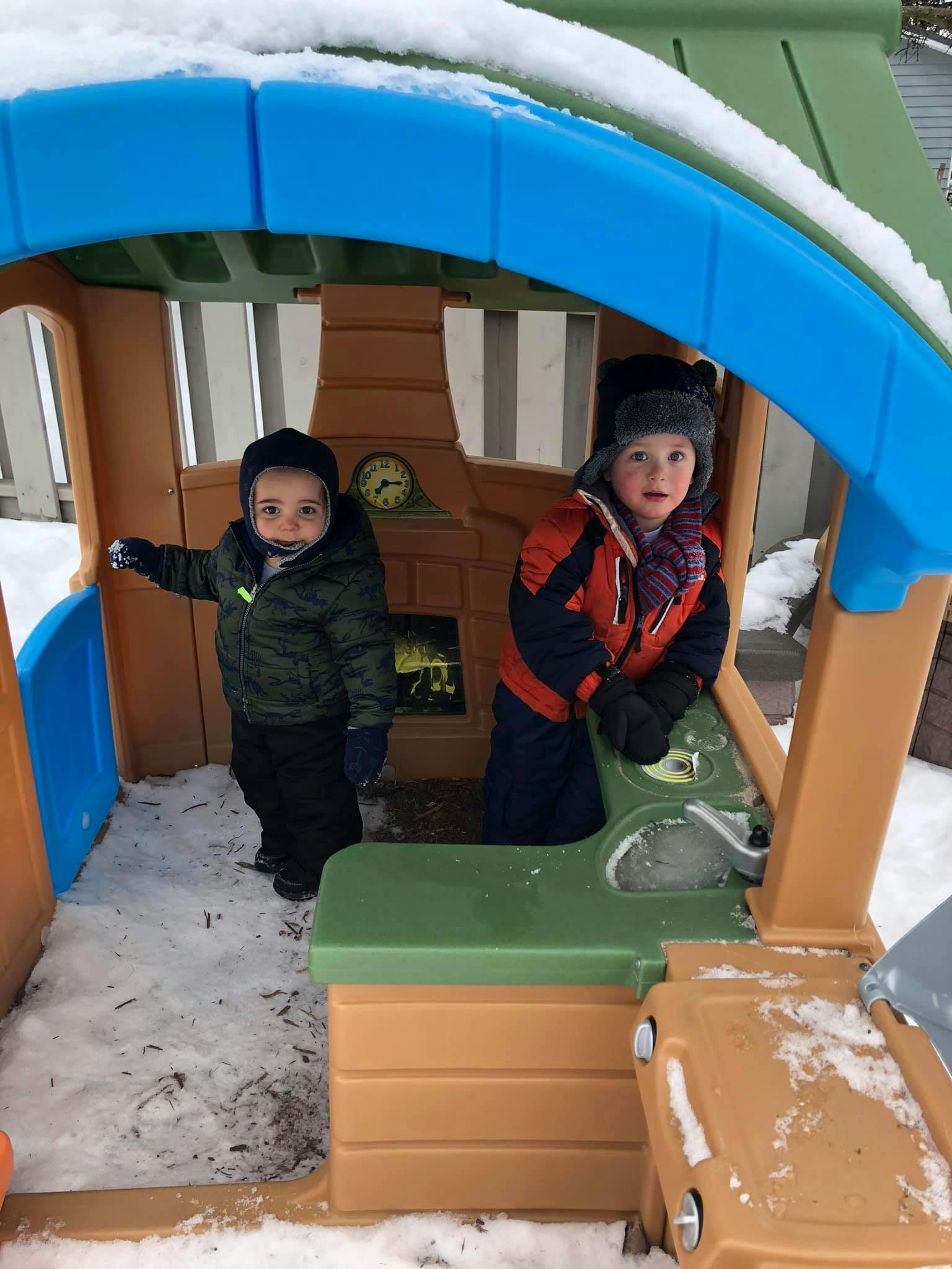 Two children in winter clothing playing in a snow-covered playhouse