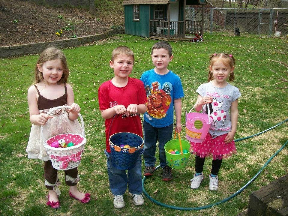 Four children holding baskets with eggs in a grassy area