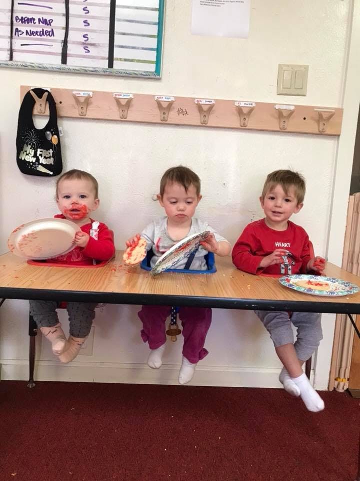 Three children sitting at a table with plates of food