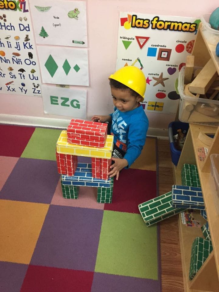 Child in a yellow hard hat playing with colorful block toys in a classroom