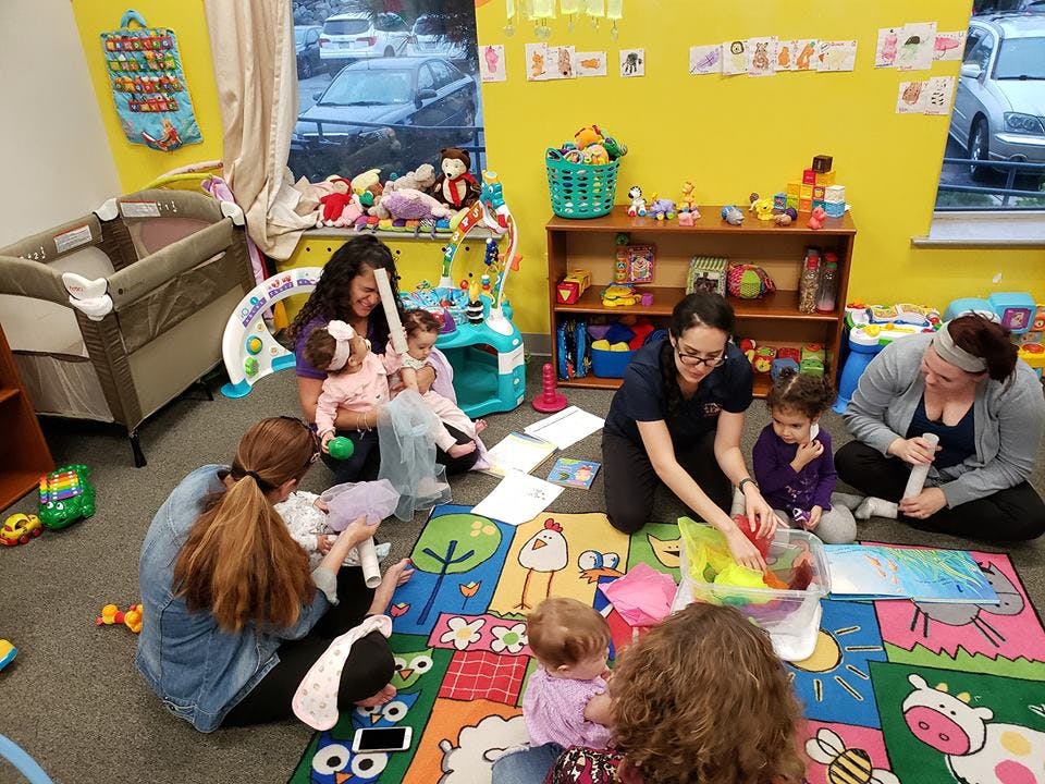 Adults and children sitting on a colorful rug in a classroom