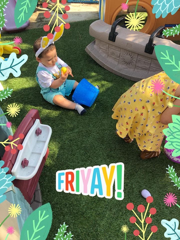 Child wearing bunny ears playing with a yellow ball and blue bucket on grass
