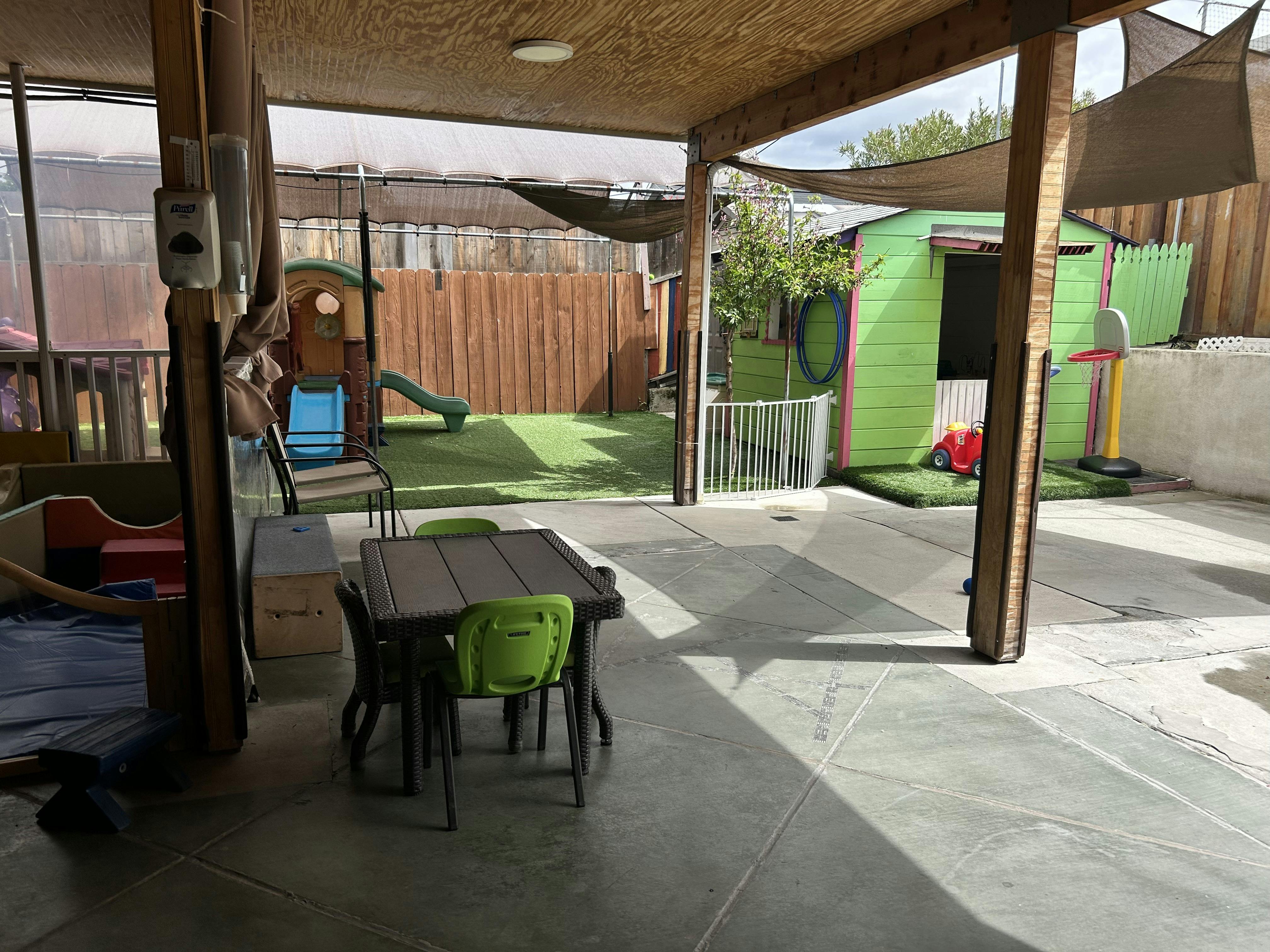 Outdoor play area with a small table and chairs, slide, and green playhouse