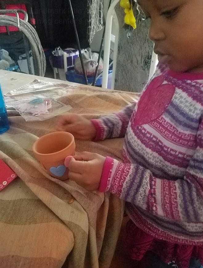 Child holding a small terracotta pot with a blue heart