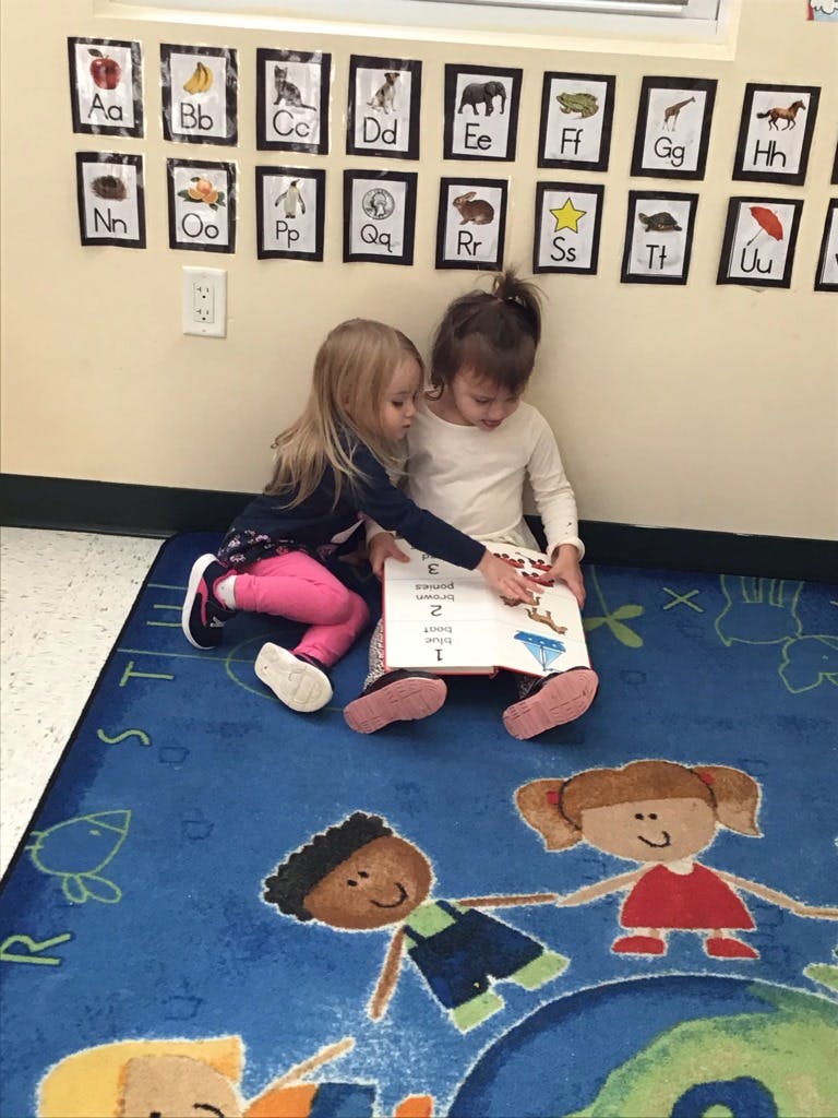 Two children sitting on a rug, looking at a book together