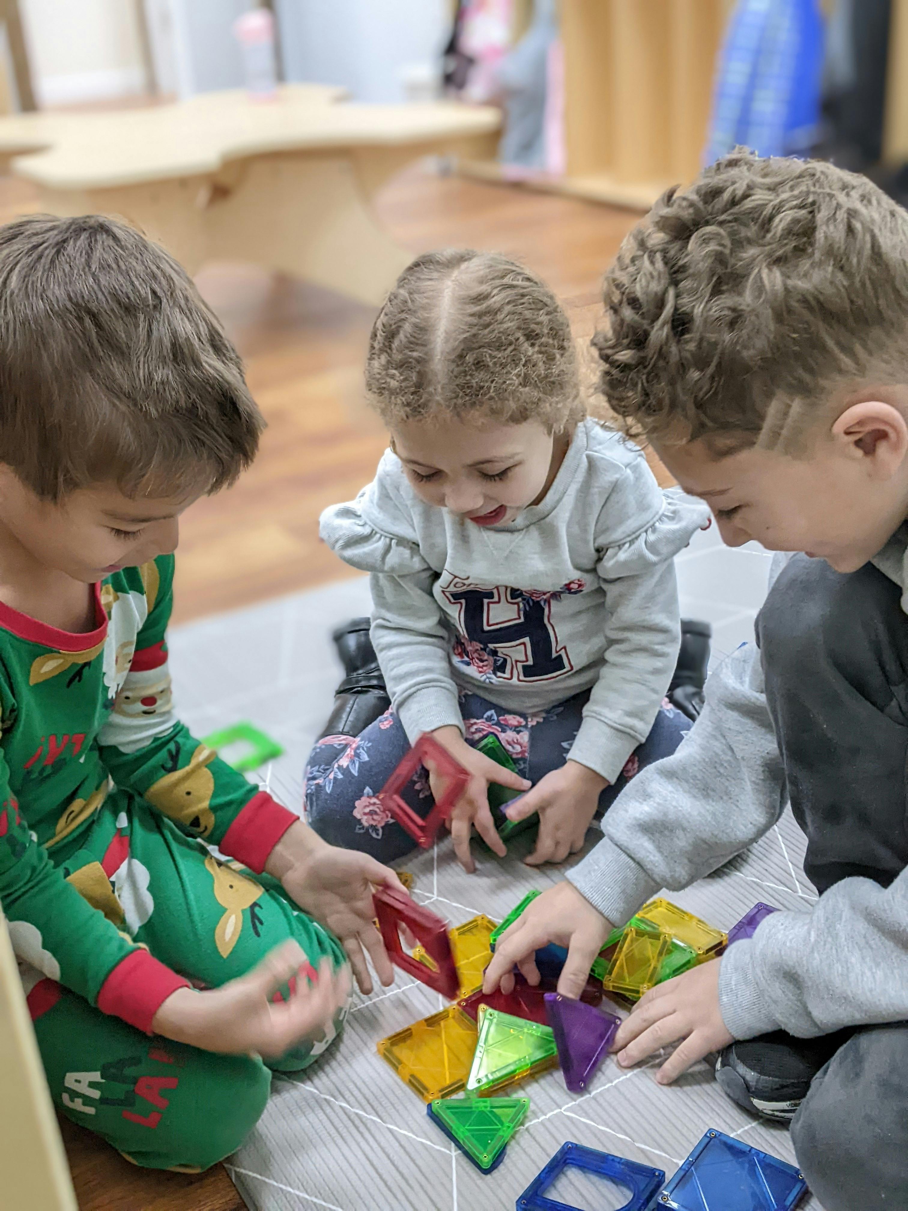 Three children playing with colorful magnetic tiles on the floor