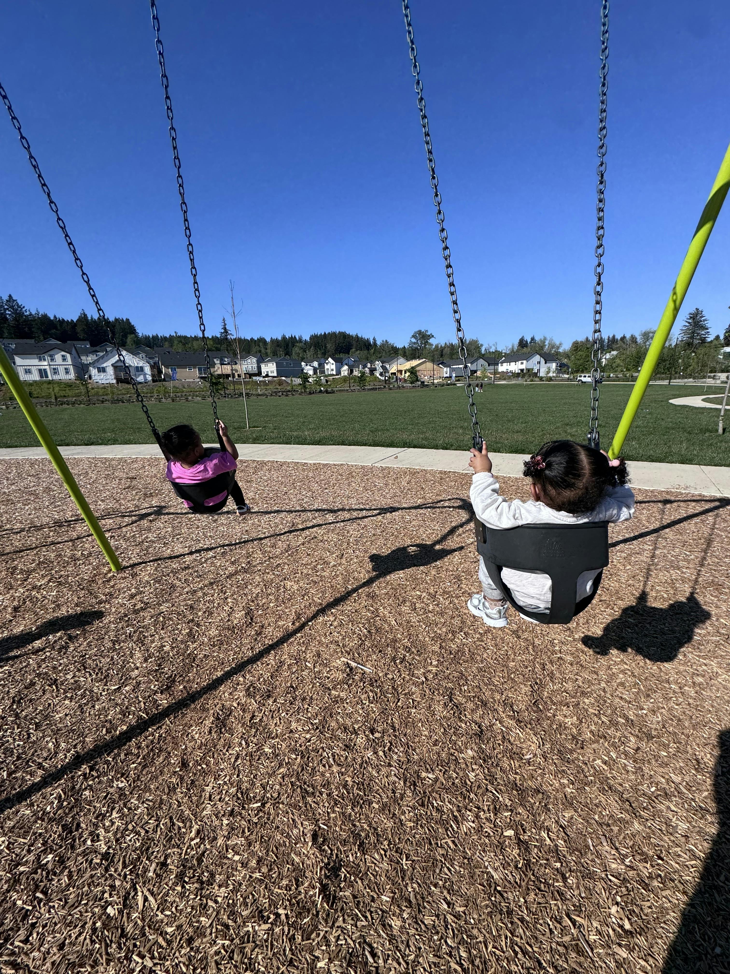 Two children swinging on a playground with houses in the background