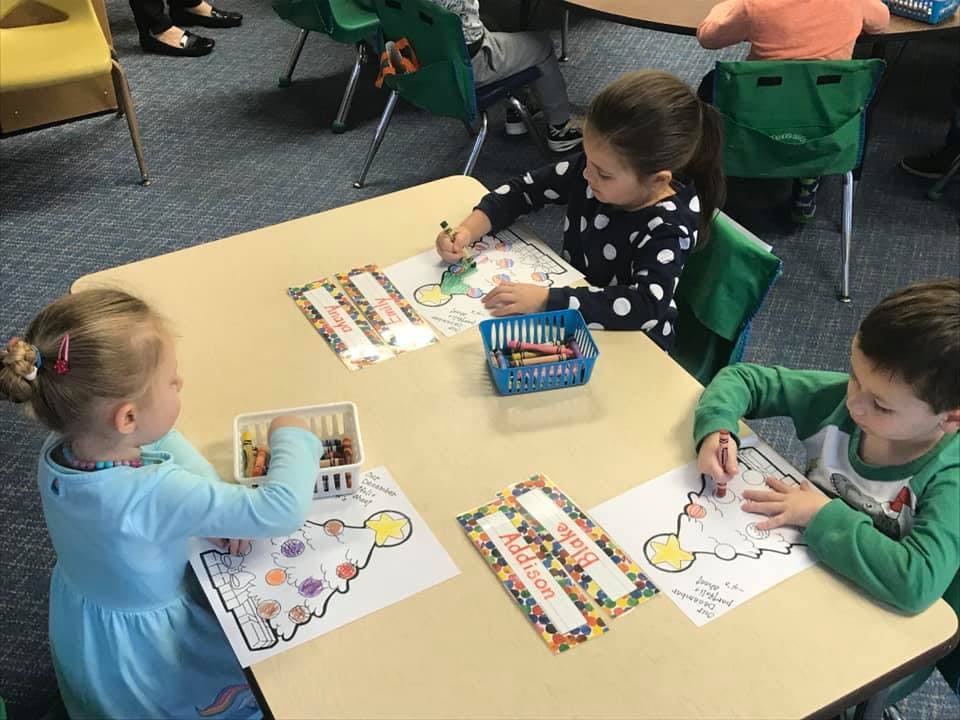 Three children coloring at a table in a classroom