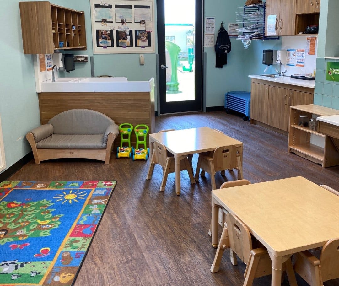 Classroom with small tables and chairs, a sink, and a colorful rug