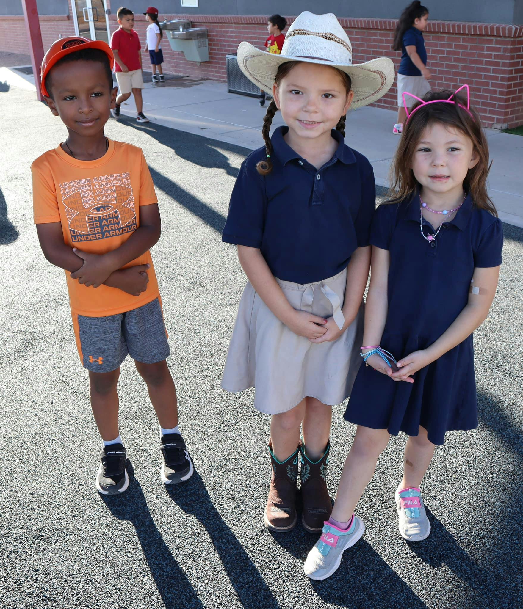 Three children standing outdoors, one wearing a cowboy hat