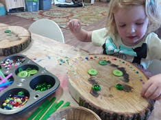 Child playing with buttons and beads on a wooden disc