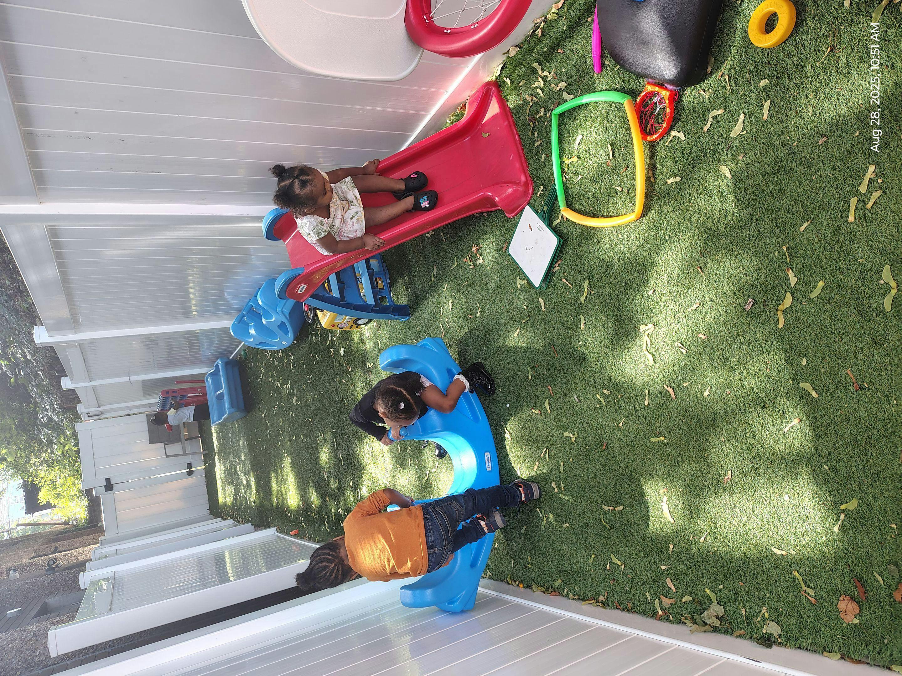 Three children playing on an outdoor playground with a slide and a rocking toy