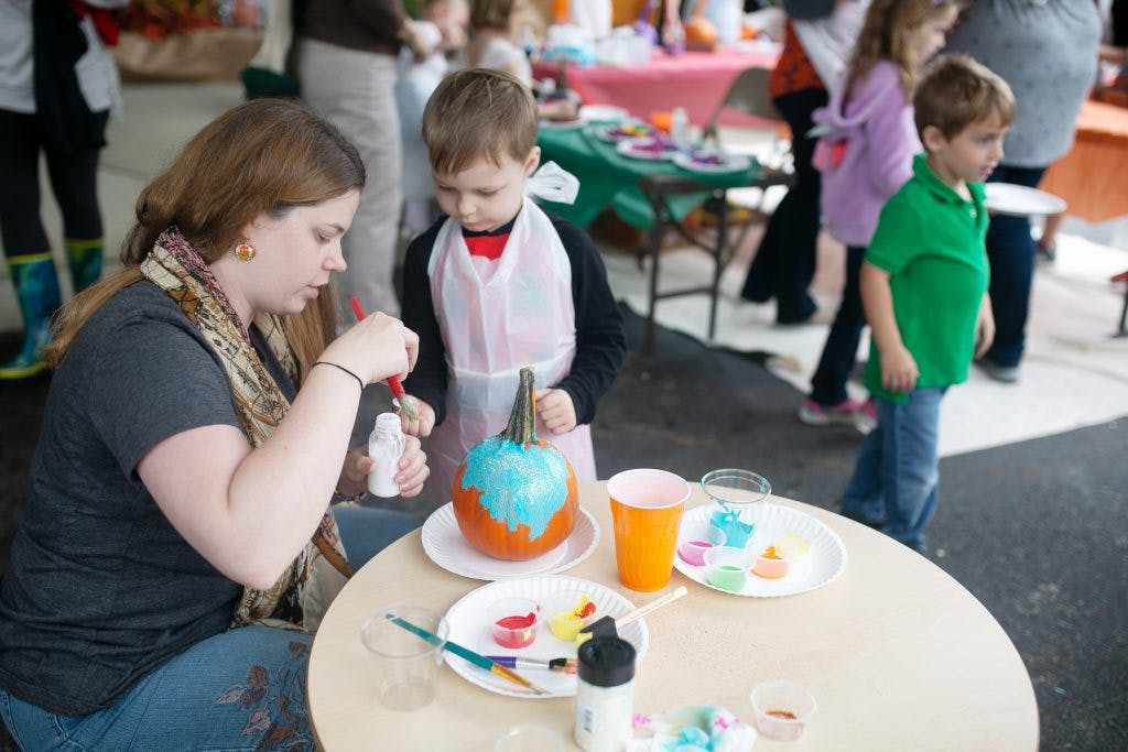 Person and child painting a pumpkin at a table