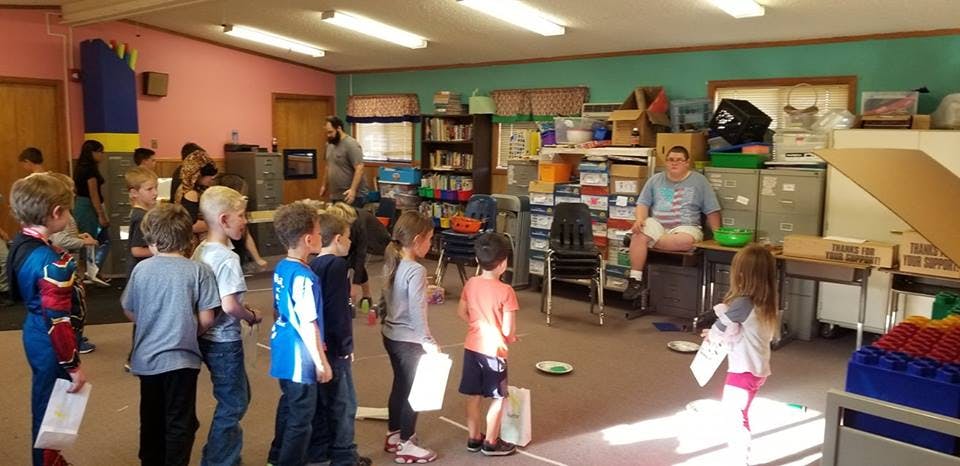 Children standing in a classroom with an adult sitting on a desk