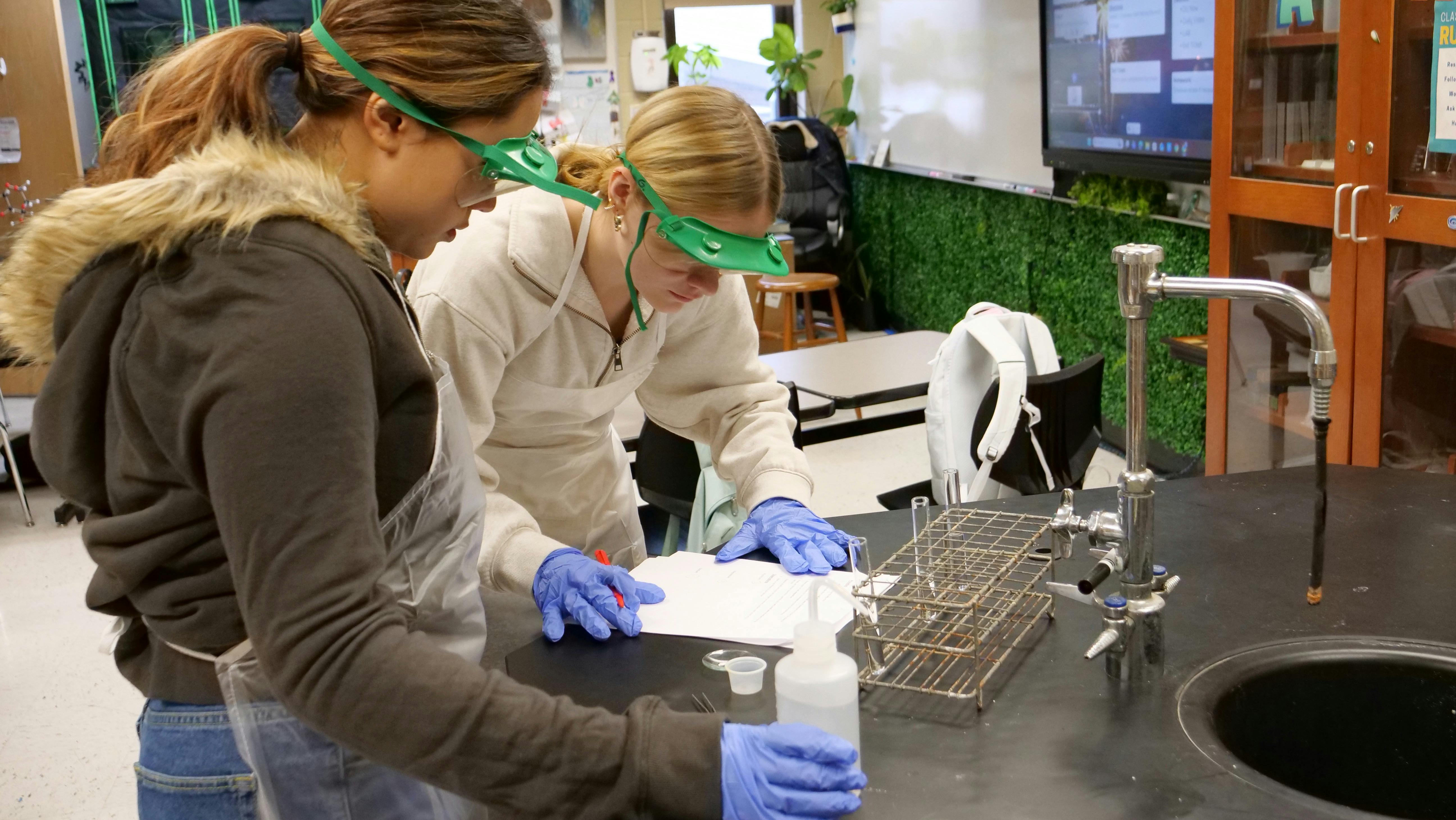 Two people wearing safety goggles and gloves working on a science experiment